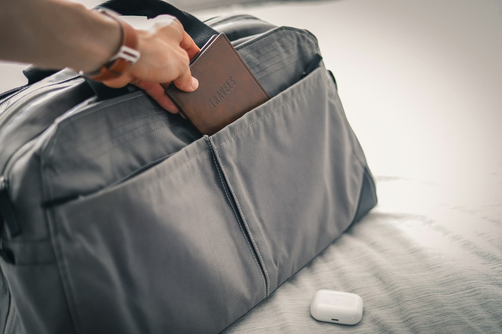 hand putting passpor tin bag with airpods on bed